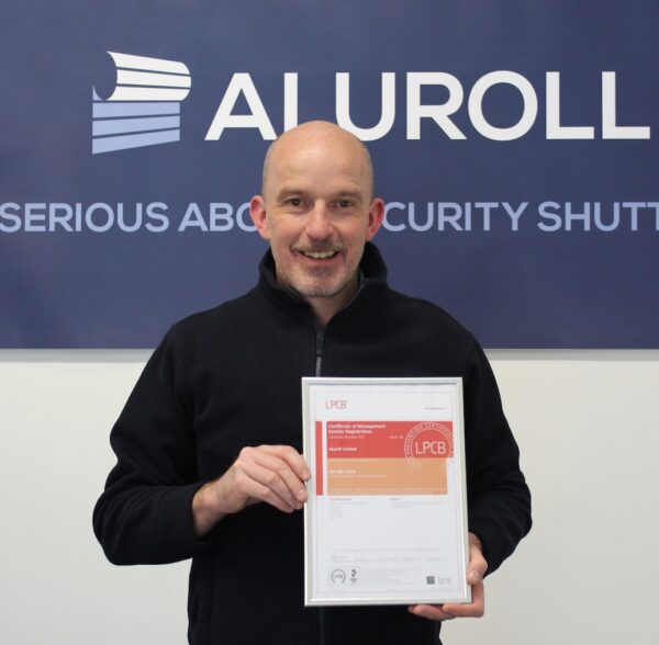 Aluroll staff member holding up LPCB approved certificate in front of Aluroll logo